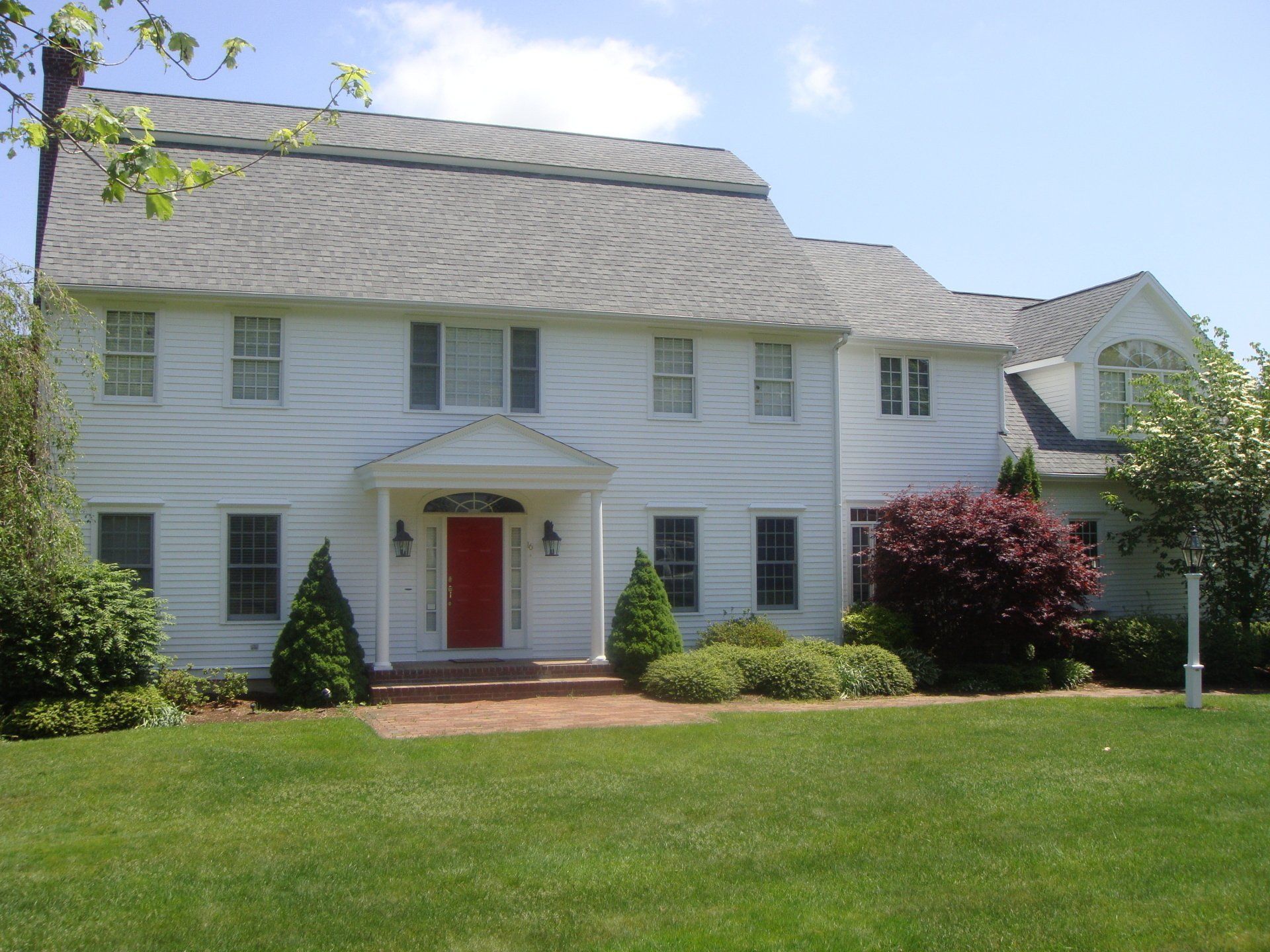 White two-story house with a red front door, white columns, and a green lawn under a blue sky