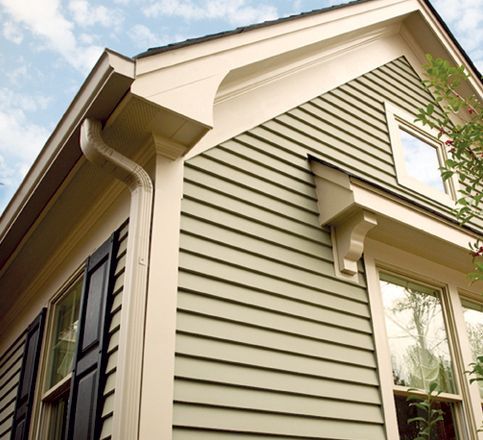 Close-up of a beige house exterior with cream trim, siding, and windows under a blue sky