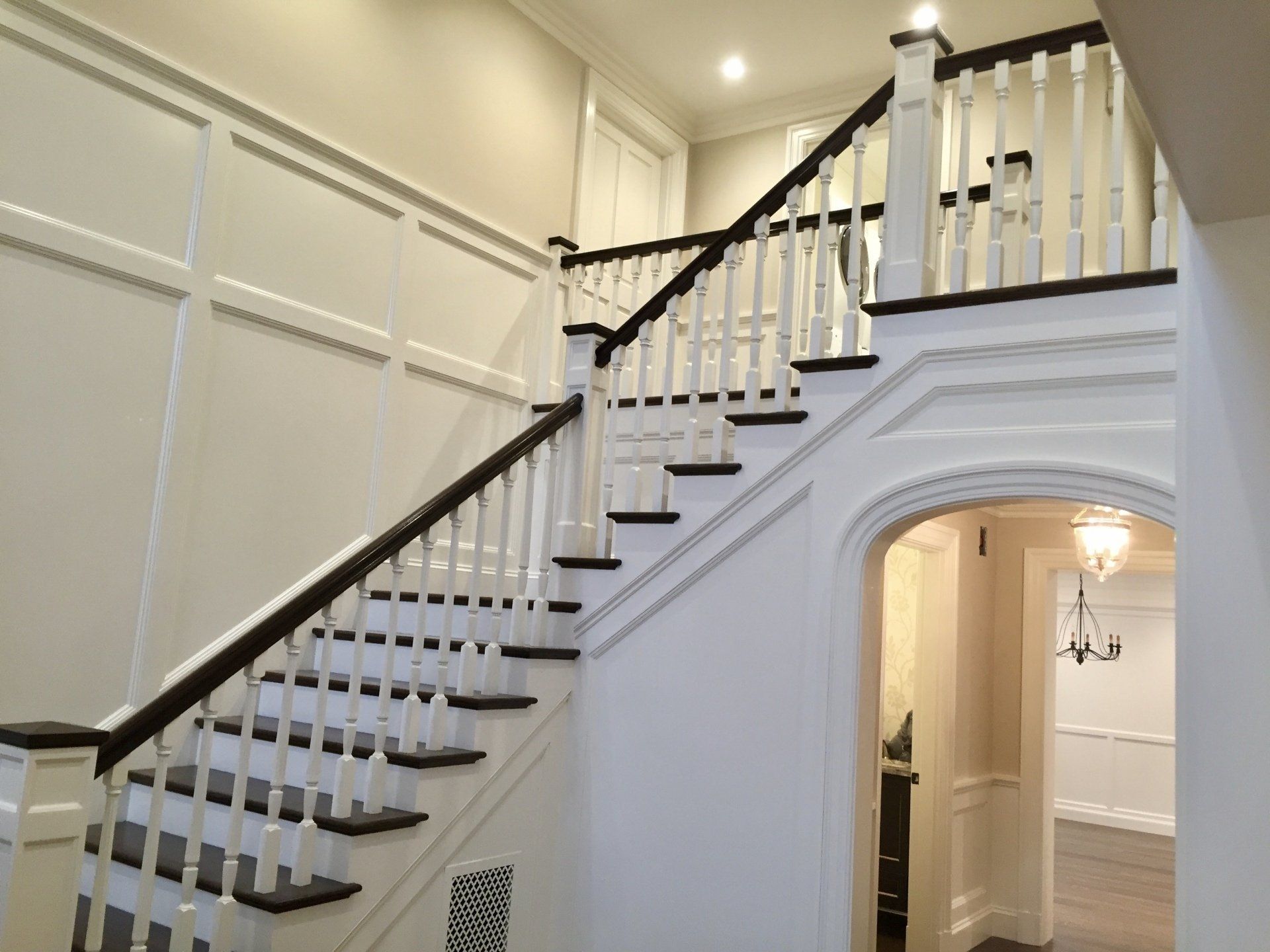 White staircase with dark wood railing in a bright hallway over an arched doorway