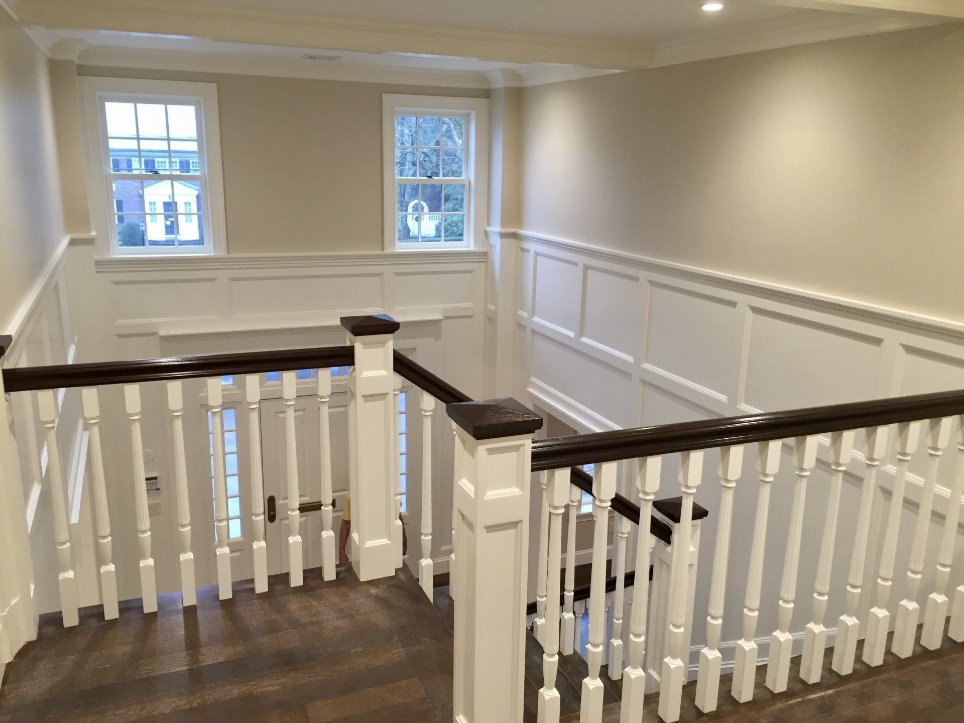 Stair landing with white railing, dark wood banister, beige walls, and two windows.