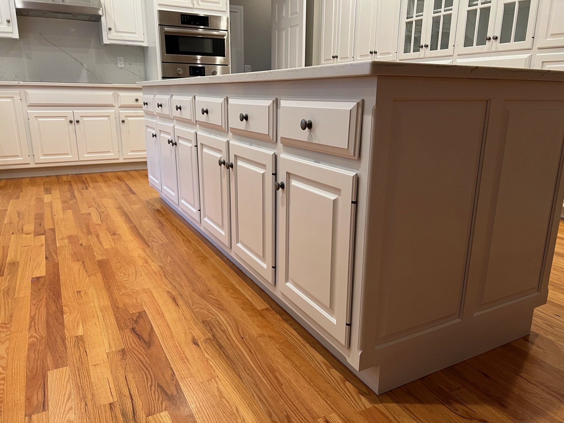 Bright kitchen with white cabinets, beige island, and warm wood flooring.