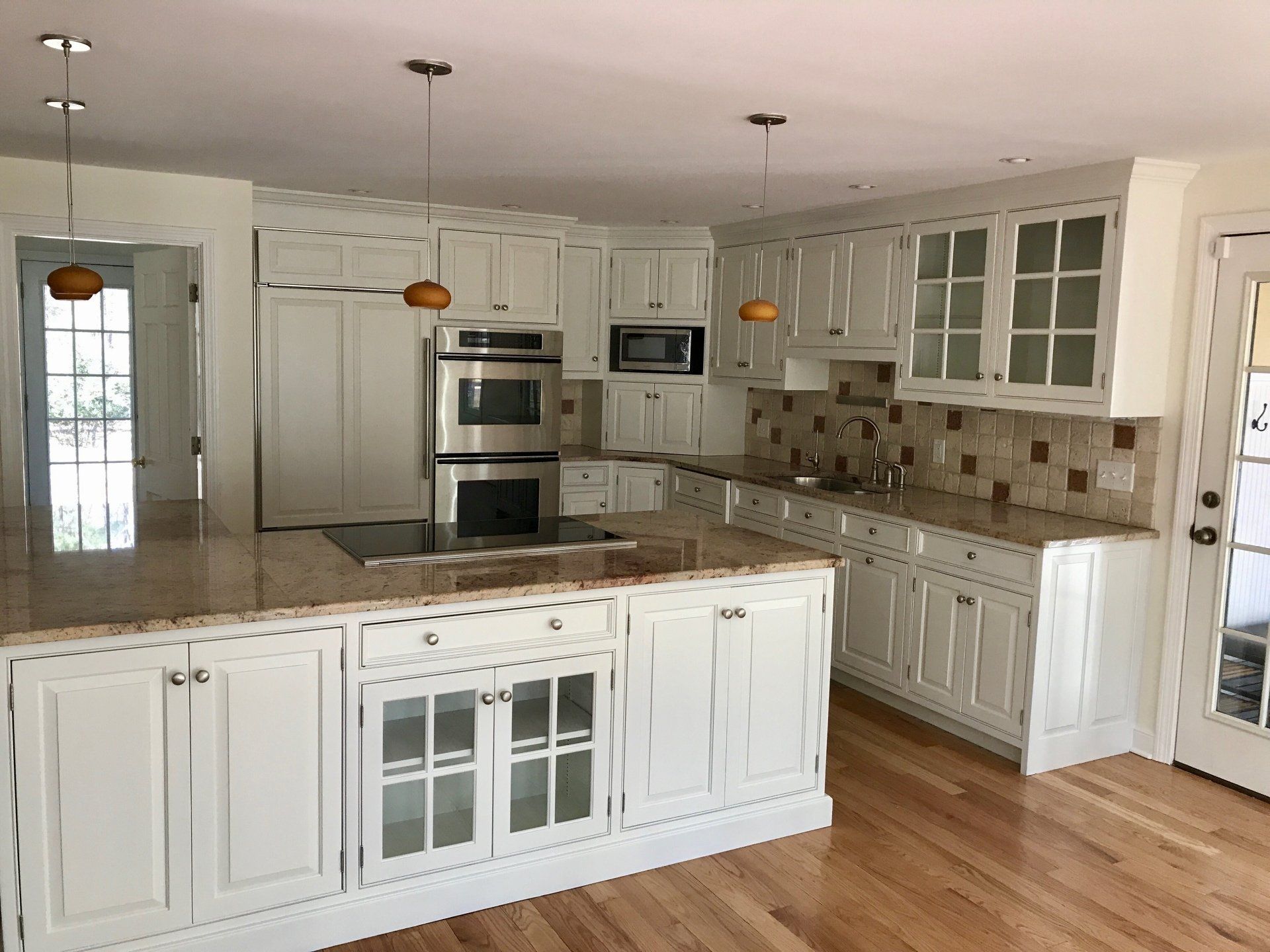 Bright white kitchen with large island, wood floor, stainless appliances, and glass-front cabinets