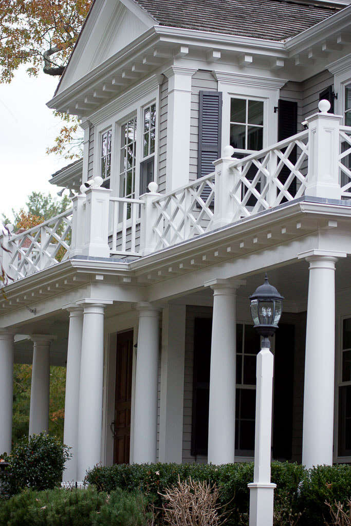 White colonial house with tall columns, black shutters, and a balcony under a striped awning