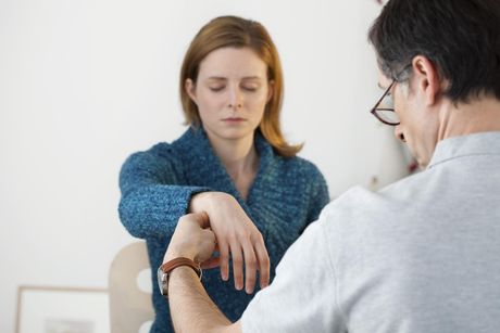 A woman is being examined by a doctor who is looking at her watch.