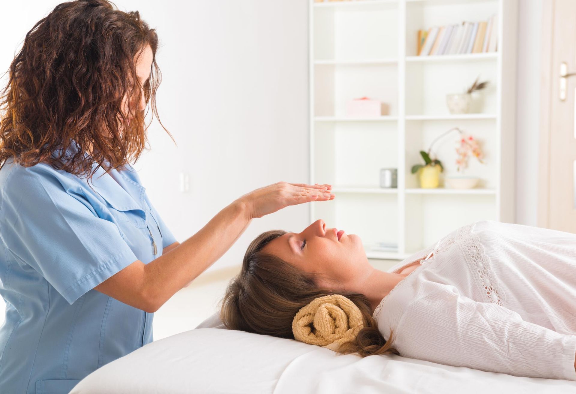 A woman is laying on a bed getting a healing treatment from a nurse.