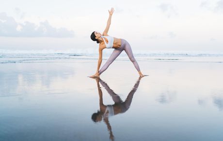 A woman is practicing yoga on the beach and her reflection is in the water.