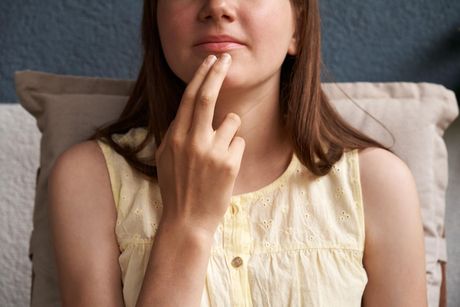 A woman is sitting on a couch with her hand on her chin.