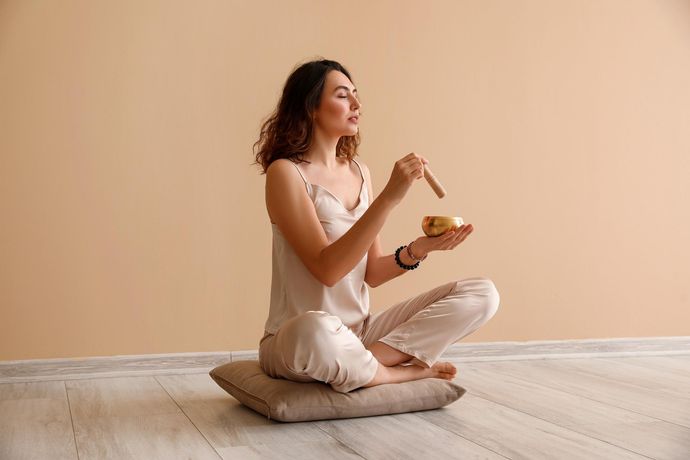 A woman is sitting on the floor with her legs crossed and holding a bowl.