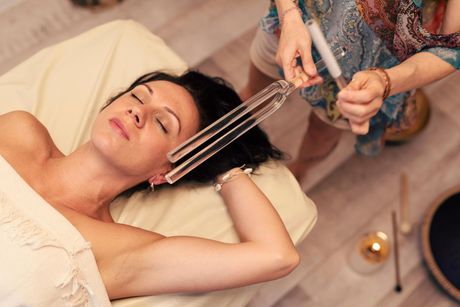 A woman is laying on a bed getting a massage with a tuning fork.