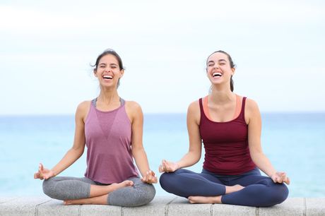 Two women are sitting in a lotus position on the beach.