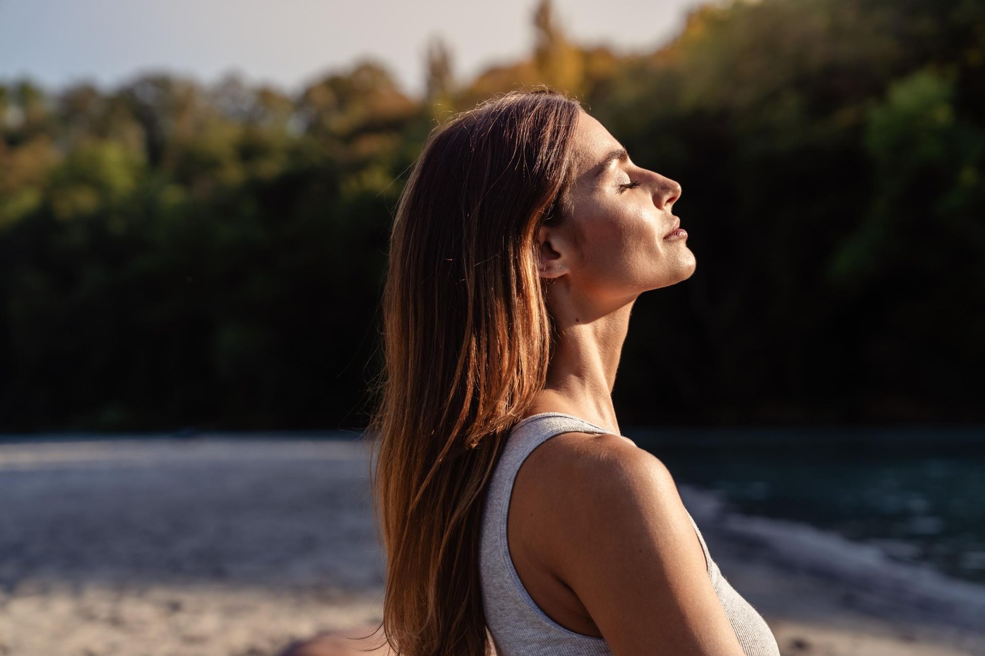 A woman is standing on a beach with her eyes closed.