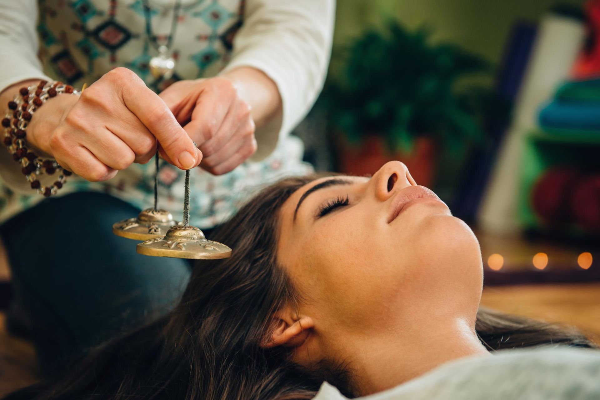 A woman is laying on the floor with her eyes closed and a person is playing a tambourine on her head.