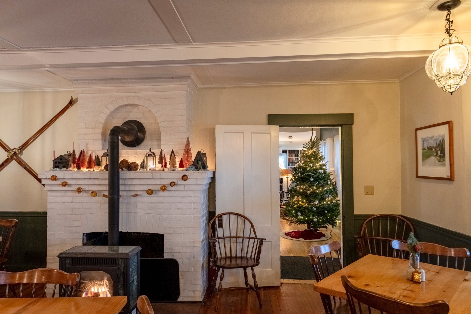 Cozy interior with fireplace, Christmas tree, wooden tables and chairs, and a decorative light.