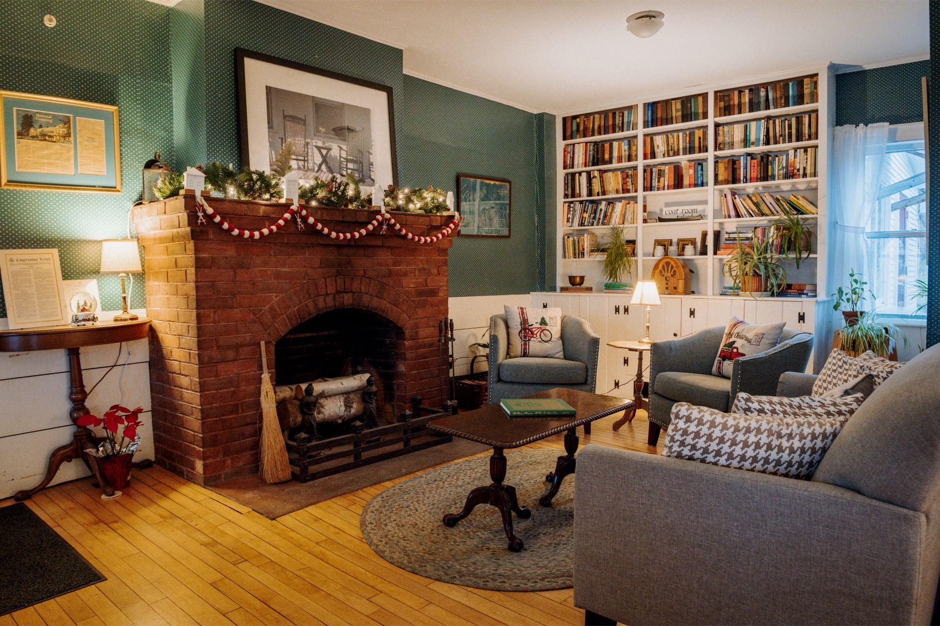 Cozy living room with brick fireplace, bookshelves, armchairs, and wood floors.