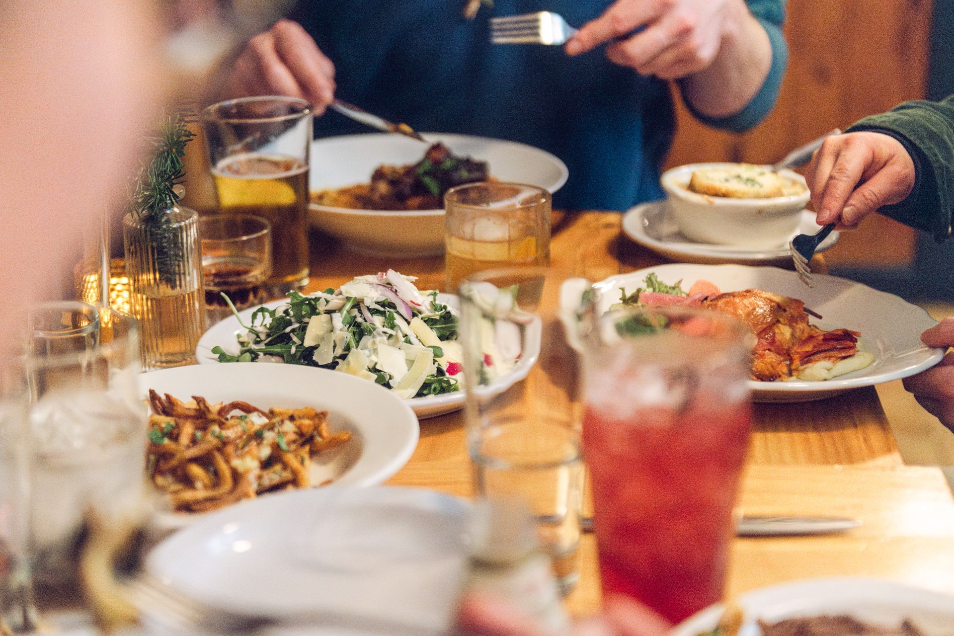People eating at a wooden table with plates of food and drinks.
