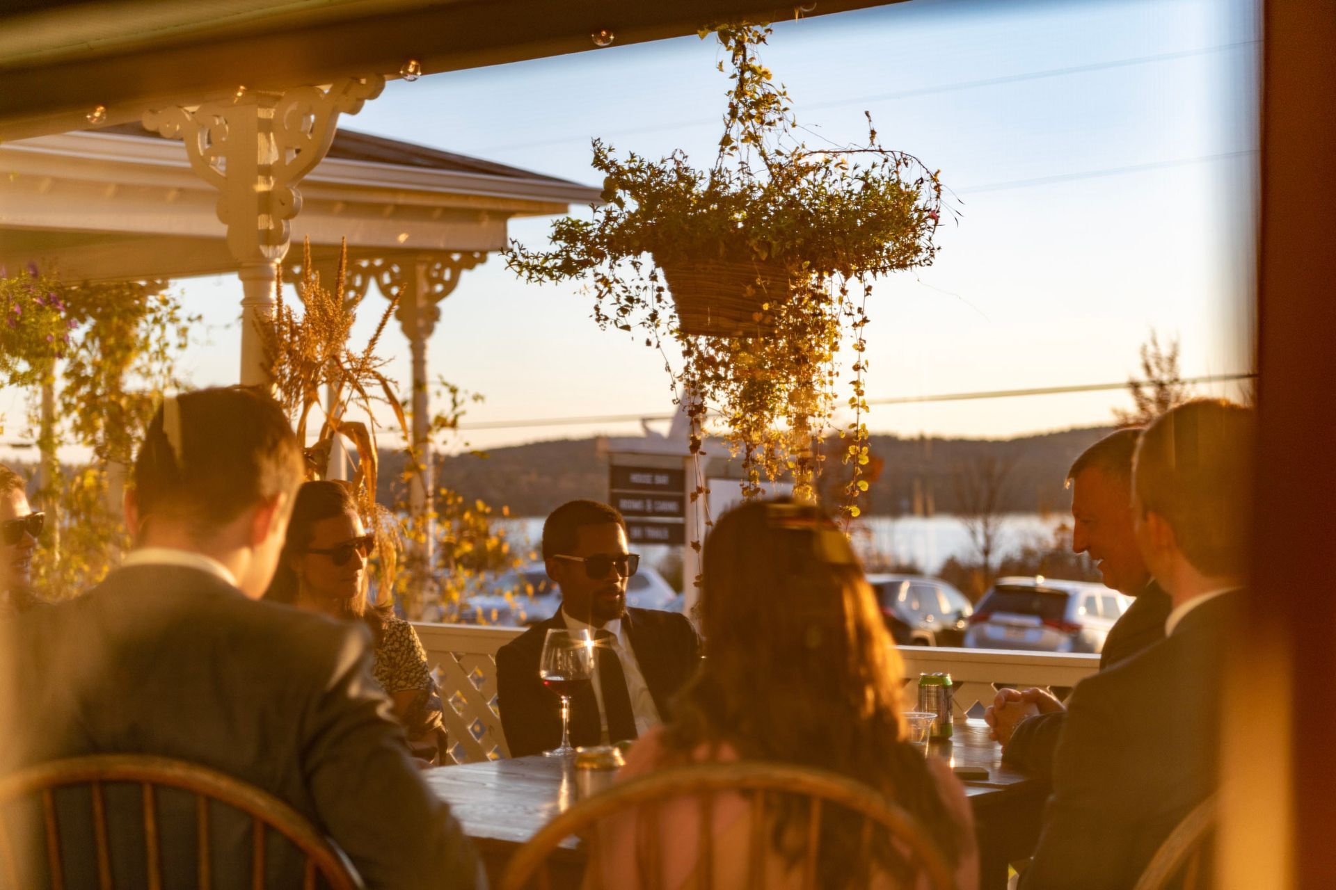 People seated at an outdoor restaurant table; waterfront view; golden hour lighting.
