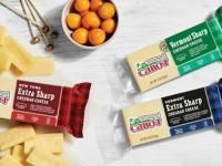 Cabot cheddar cheese blocks and bowl of orange fruits on a white surface.