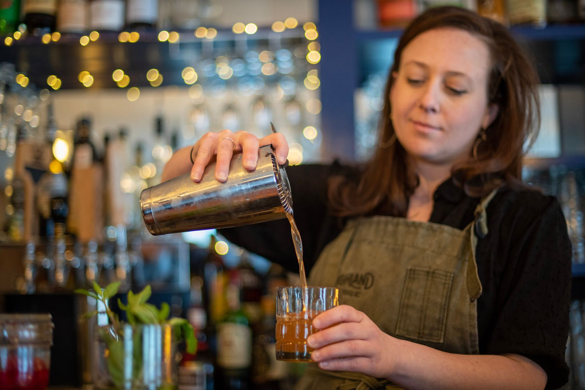Bartender pouring drink from shaker into glass; bar setting.