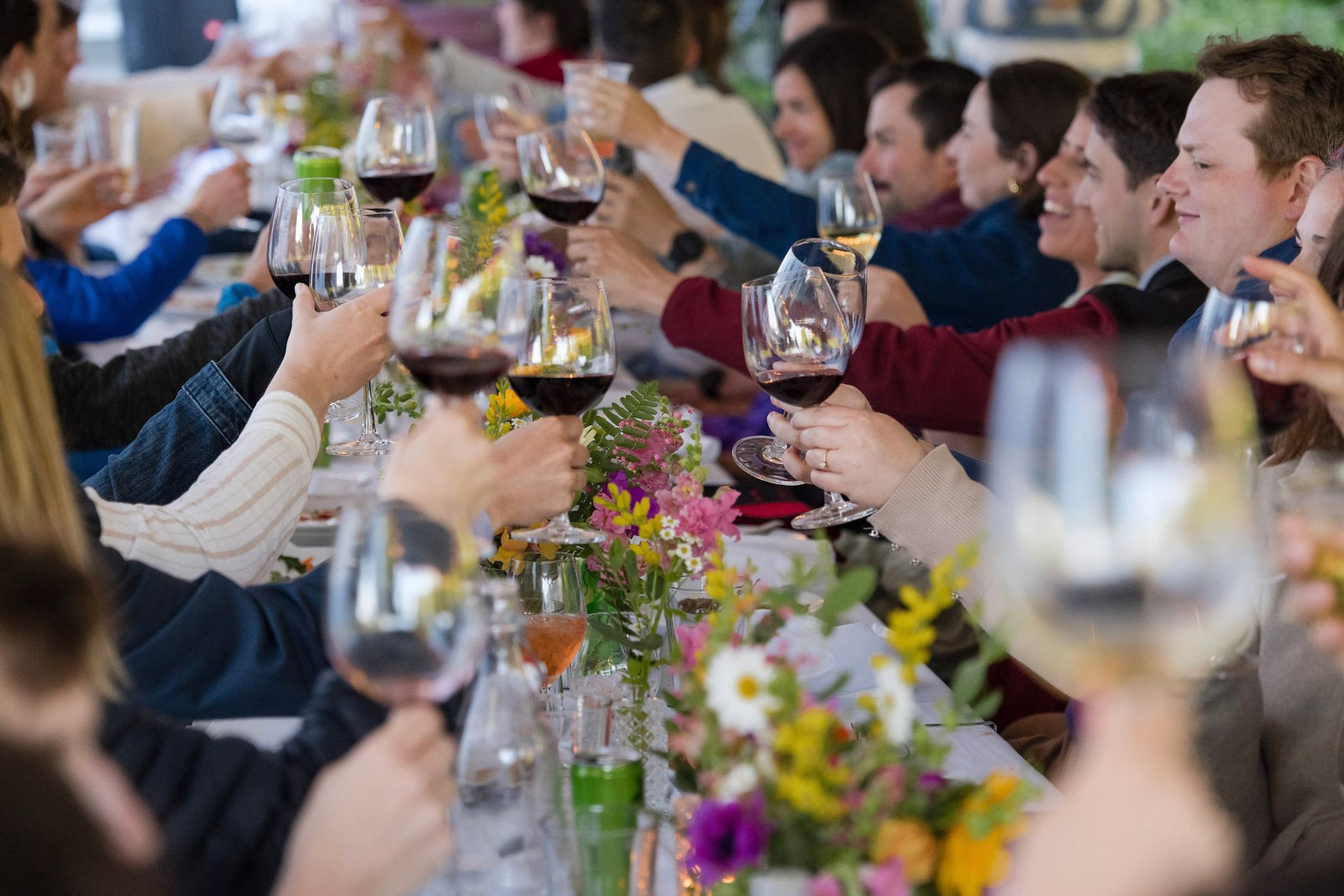 People toasting with wine glasses at a long table with flowers.