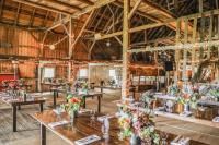 Rustic barn interior, tables set for a gathering, floral centerpieces. Wooden beams and warm lighting.
