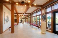 A bright, open hallway with wooden beams, large windows, and benches, offering views outside.