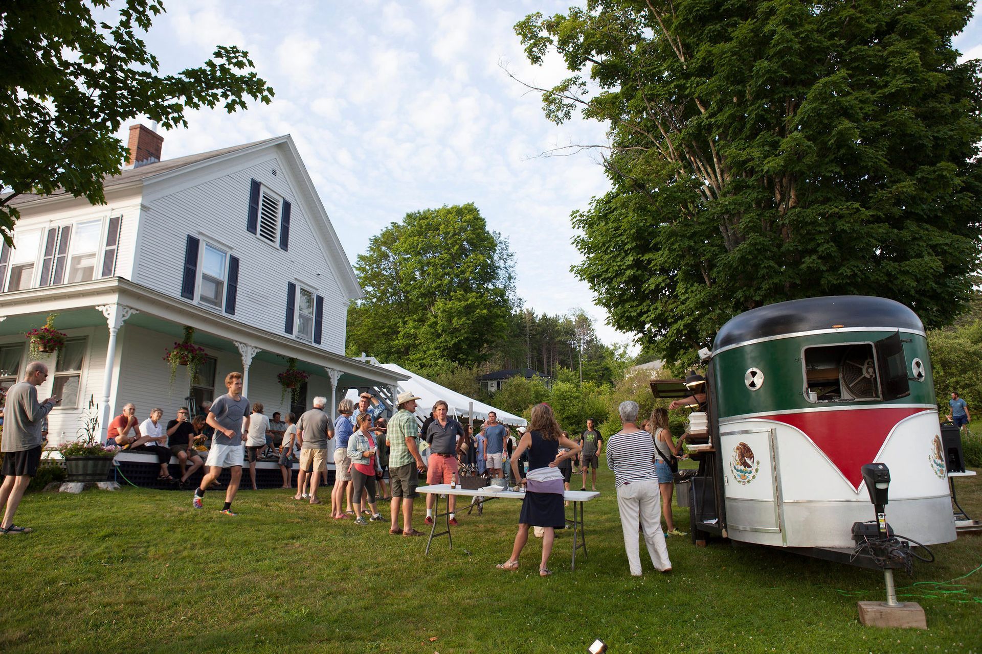 People gathered outside a white house with a food truck.