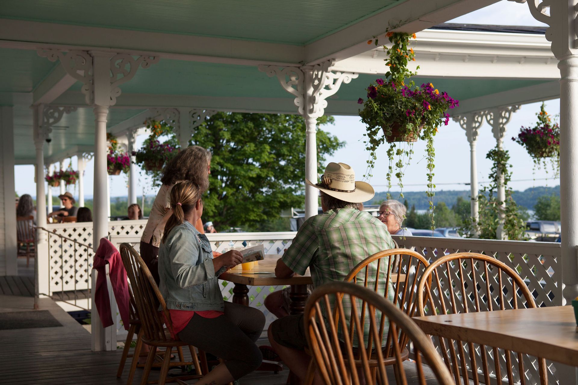 People seated at outdoor cafe tables with hanging flower baskets.