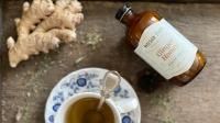 Ginger honey tea preparation: fresh ginger, honey bottle, cup with floral saucer, tea pouring.