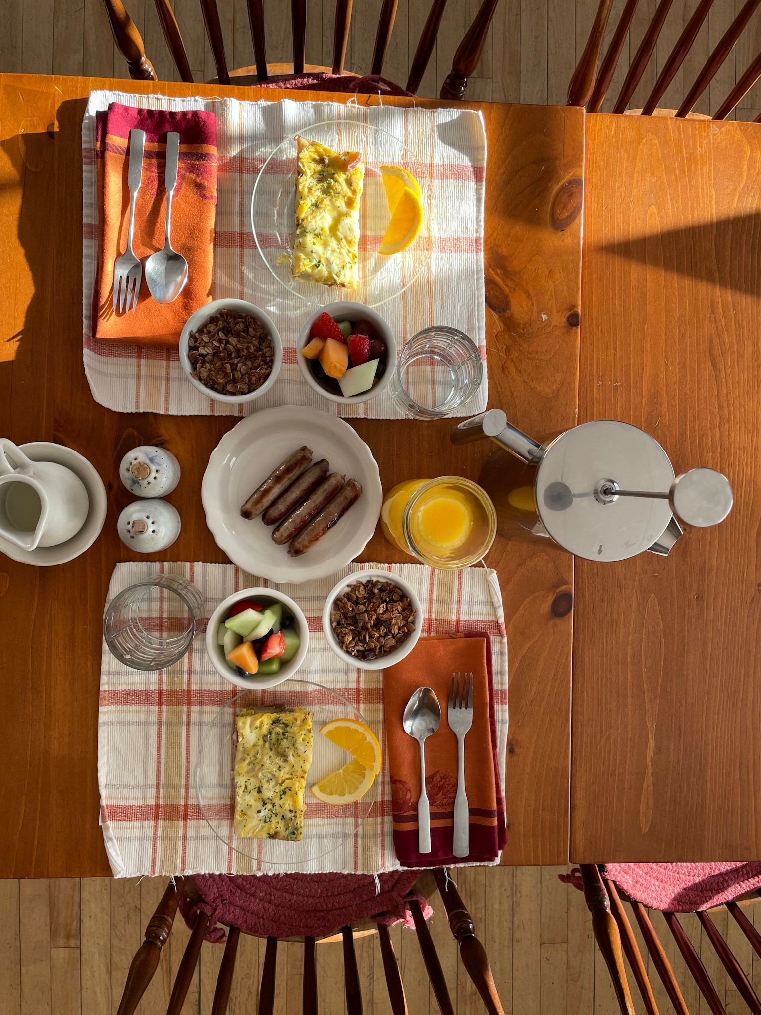 Two breakfast settings on a wooden table, each with omelet, fruit, sausage, and coffee.