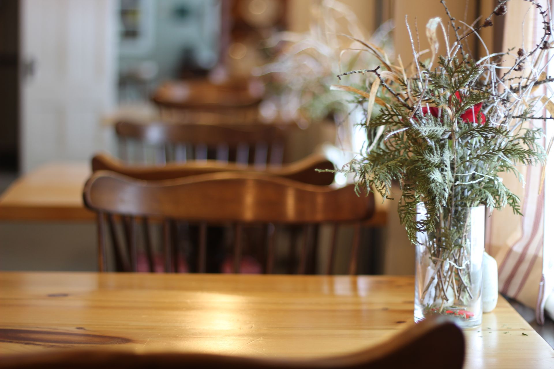 Wooden tables and chairs in a cafe, with a vase of flowers on a table in the foreground.