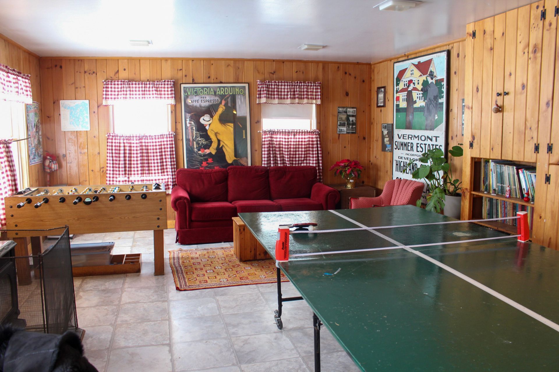 Recreation room with foosball, ping pong, red sofa, and art on wood paneled walls.