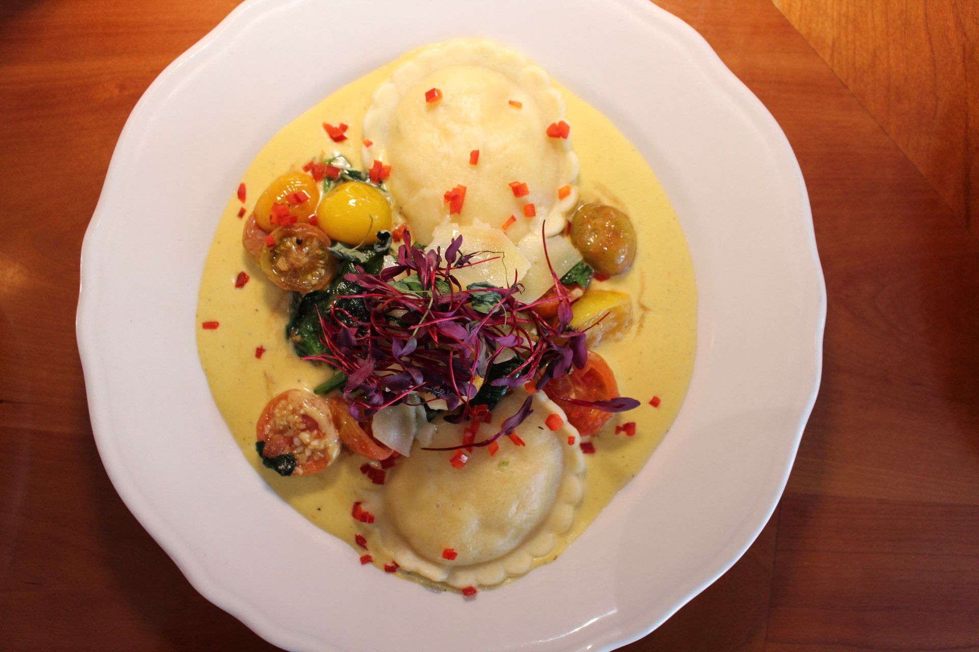 Ravioli on a plate with yellow sauce, tomatoes, and red cabbage.