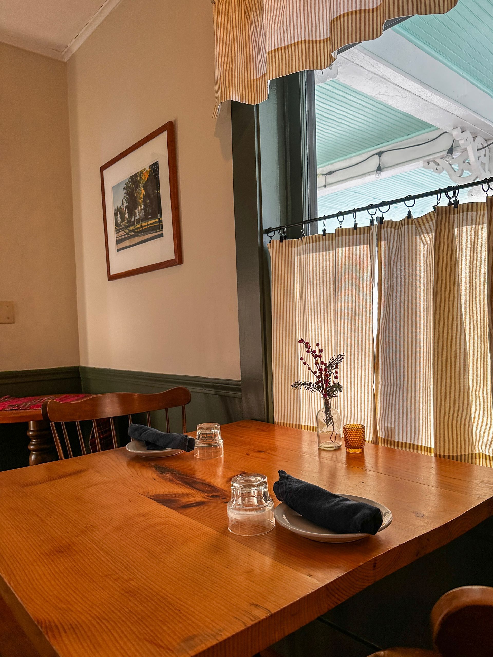 Wooden dining table set by a window with striped curtains, restaurant setting.