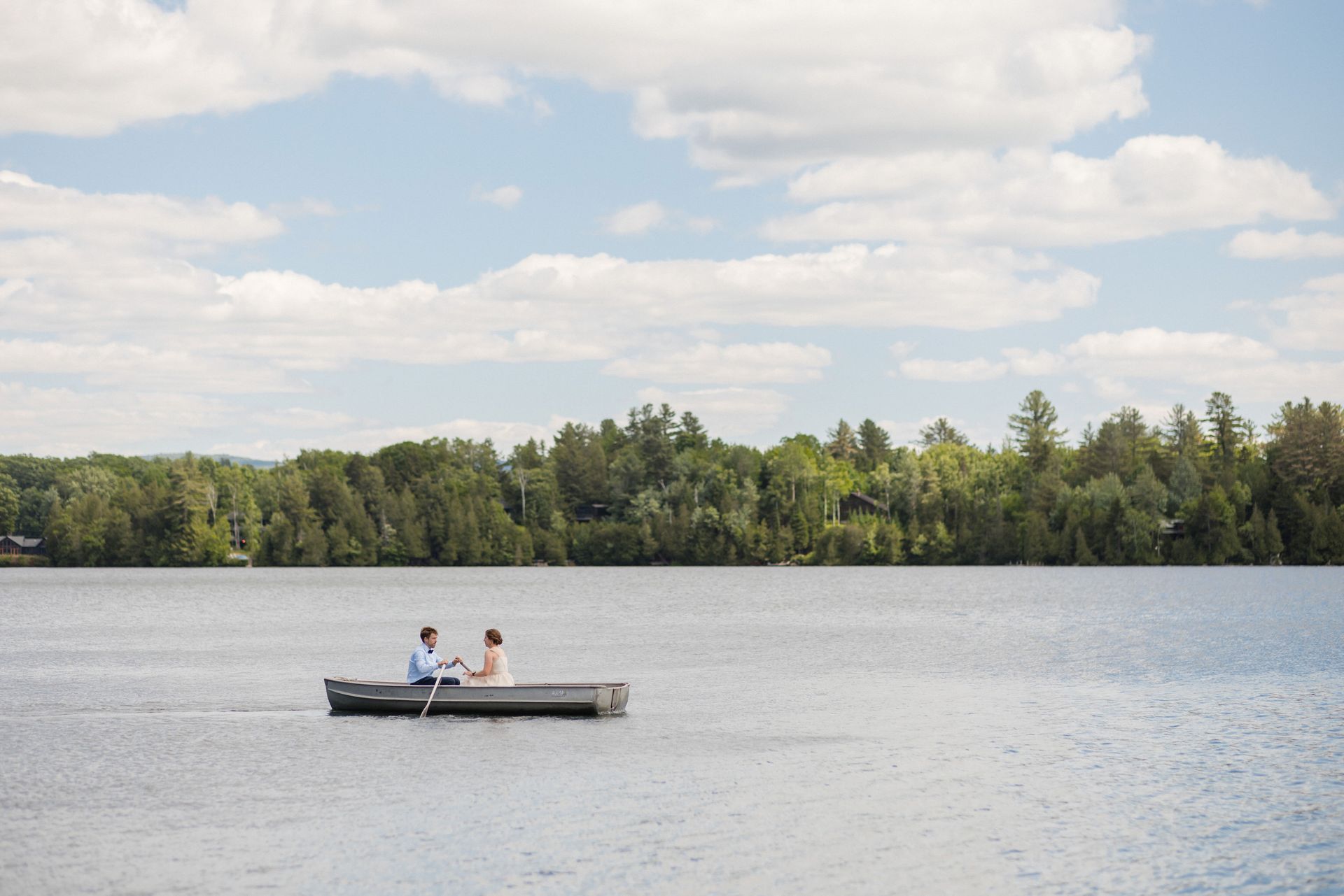 Couple in a rowboat on a lake with trees in the background under a cloudy sky.