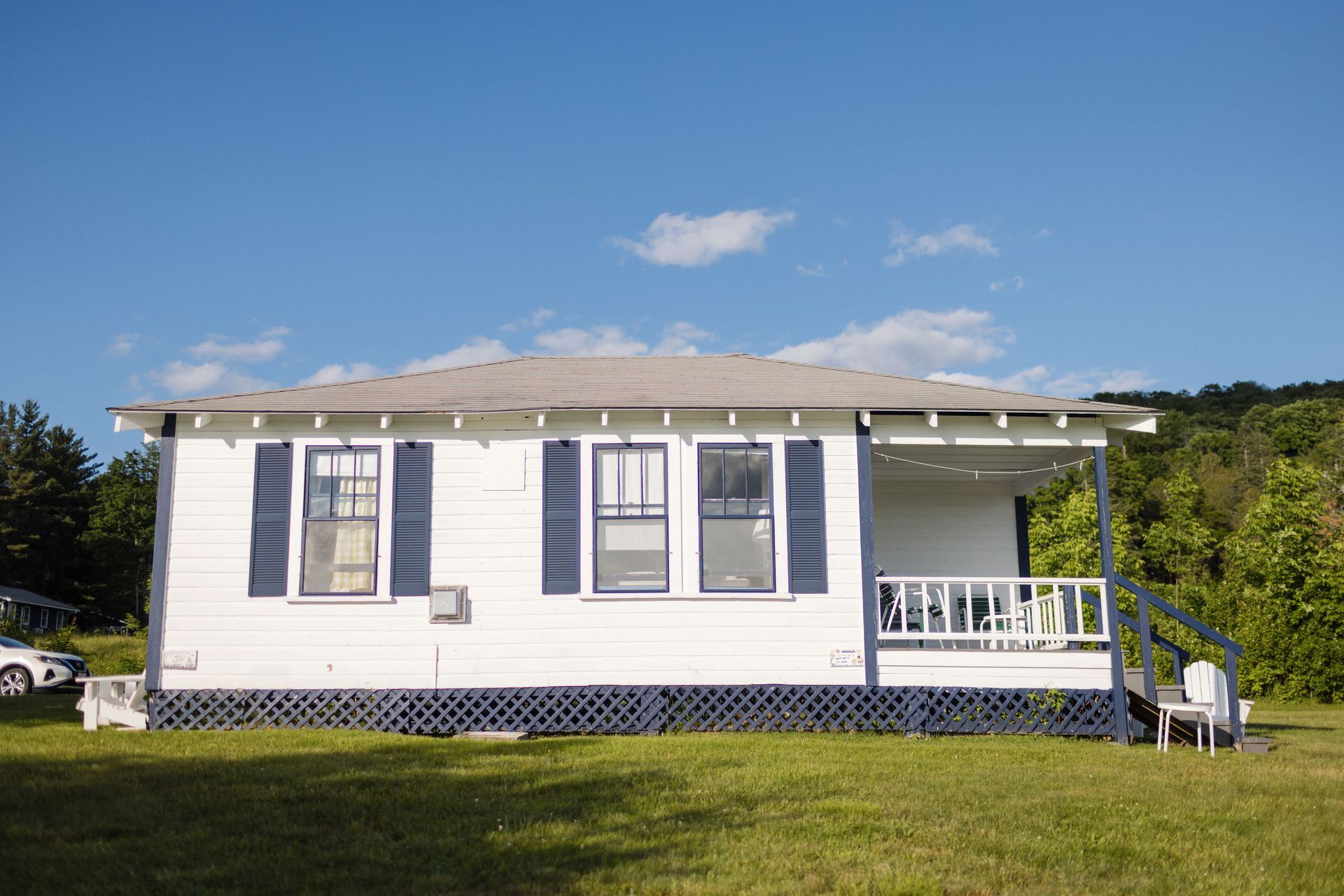 White house with blue trim, small porch, and shutters, under a blue sky, on a grassy lot.