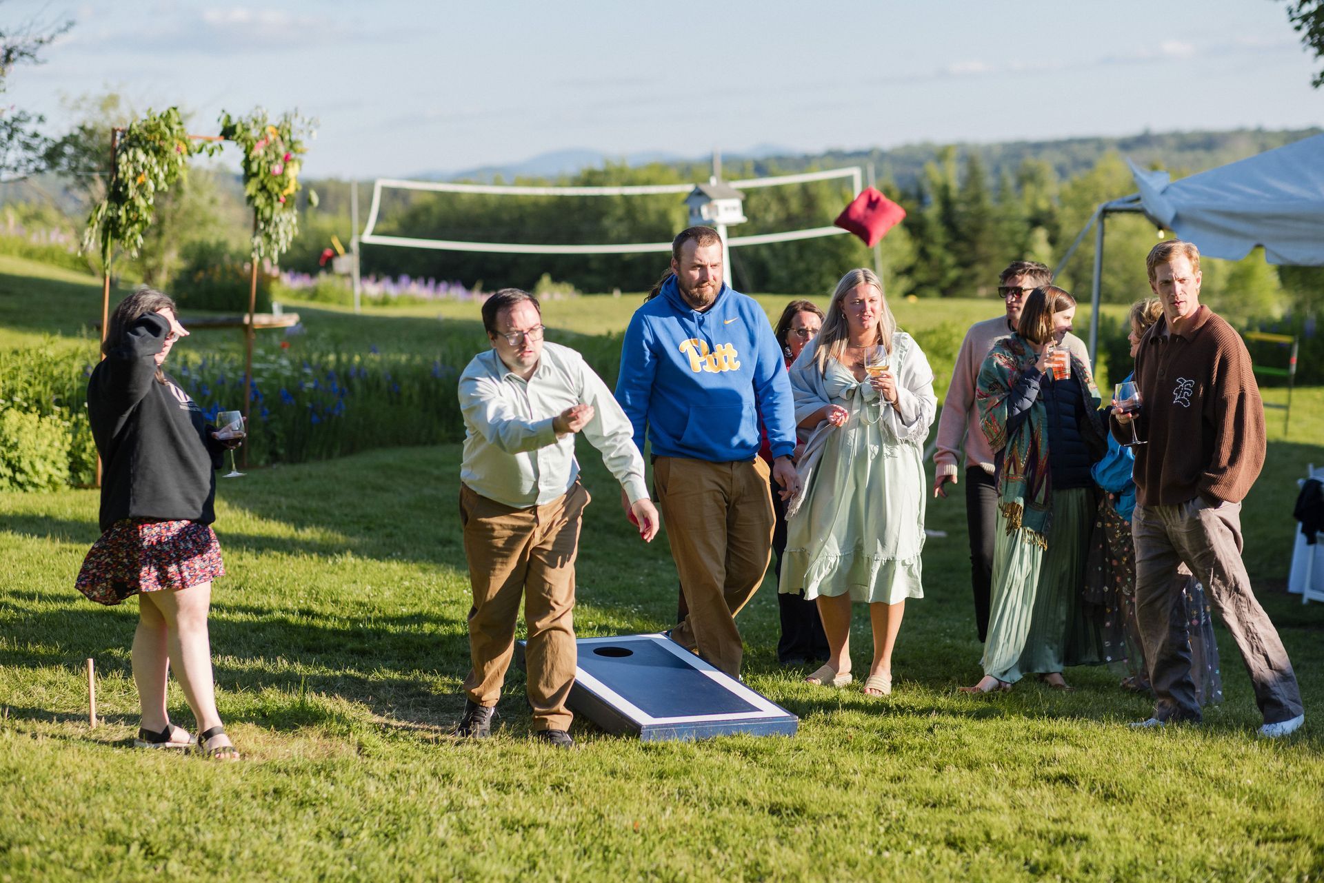 People playing cornhole on a grassy hill. One throws a beanbag, others watch.