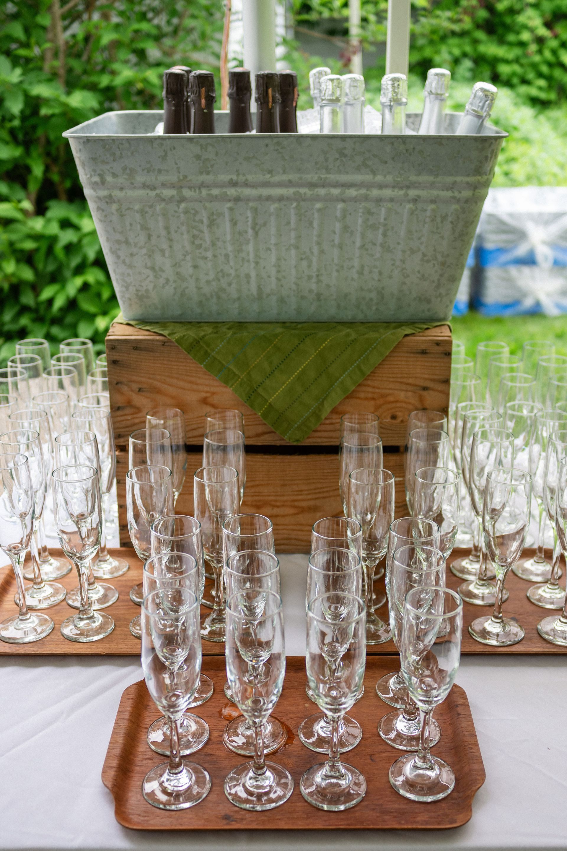 Champagne flutes on trays, ice bucket with bottles, and a green napkin, outdoor setting.