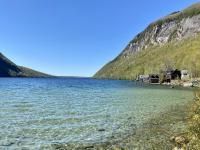 Clear lake surrounded by mountains on a sunny day. Old wooden buildings on the shore.