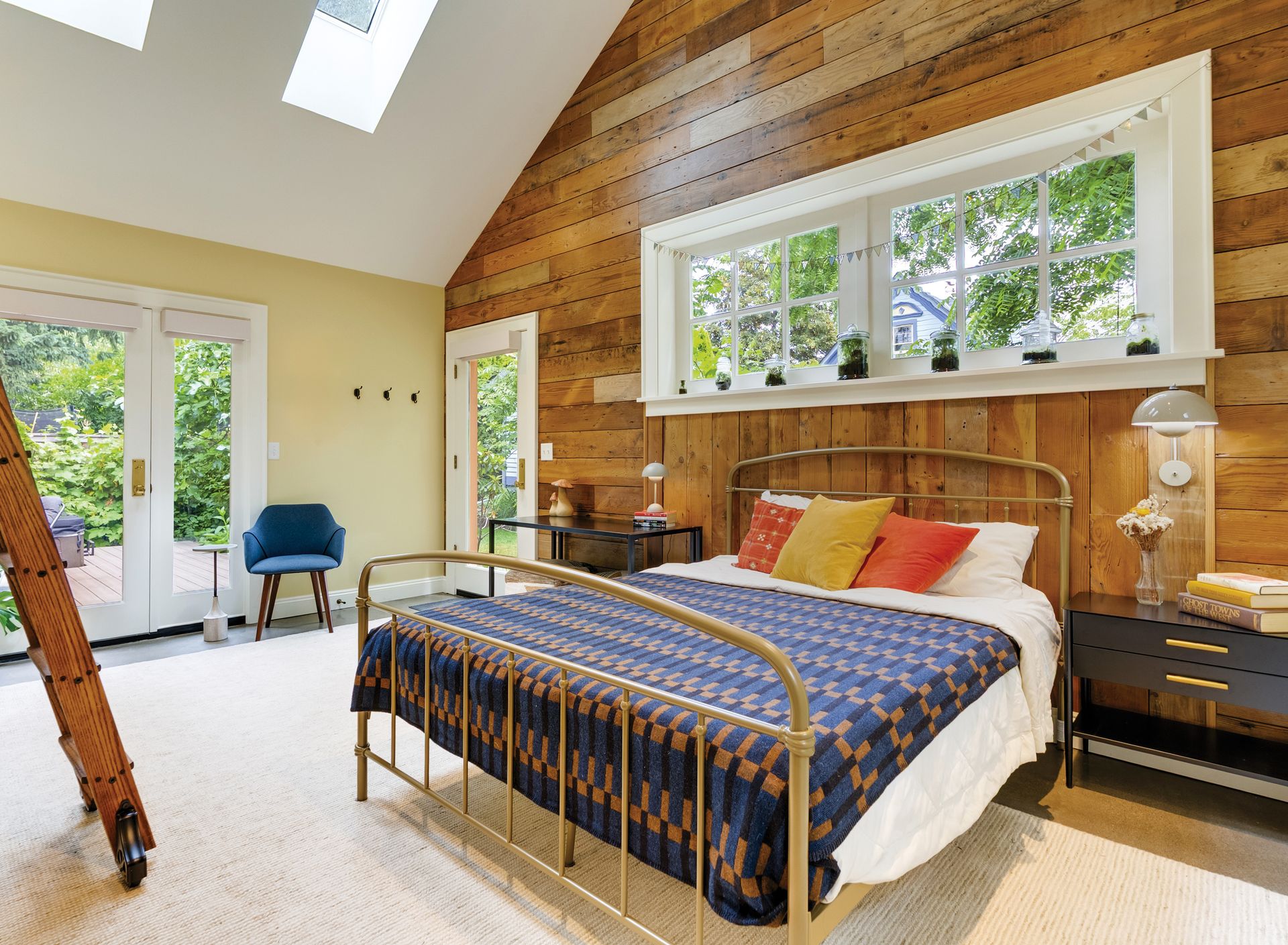 The garage-turned-studio's window wall, clad in horizontal wood paneling sits behind a cozy bed under a skylight.