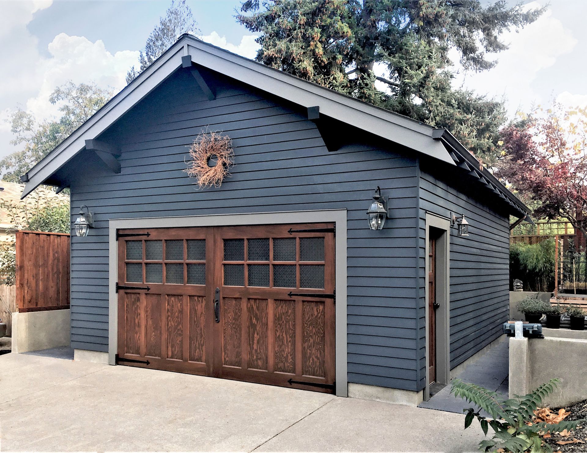 A completely restored garage in sophisticated blue and gray hues with custom stained carriage doors flanked by a pair of lanterns.