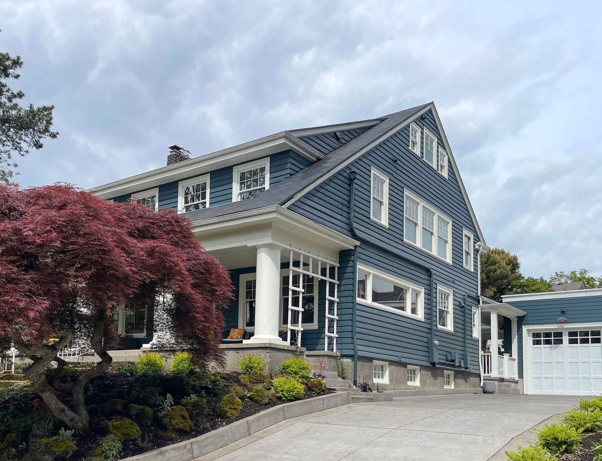 View from the driveway of a handsome Dutch Colonial home in blue gray with white trim and prominent porch columns.