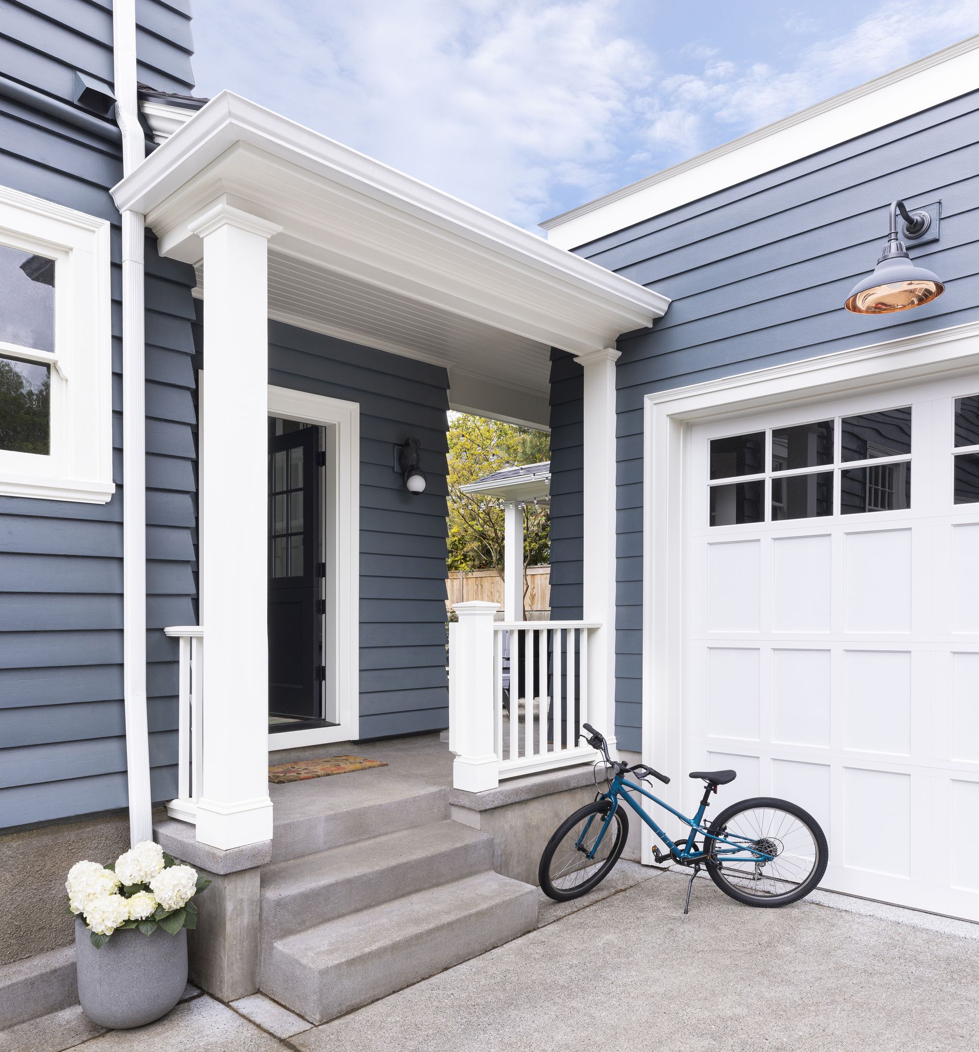 Looking at the exterior of the mudroom from the driveway with the garage to the right in blue gray with white doors and trim.