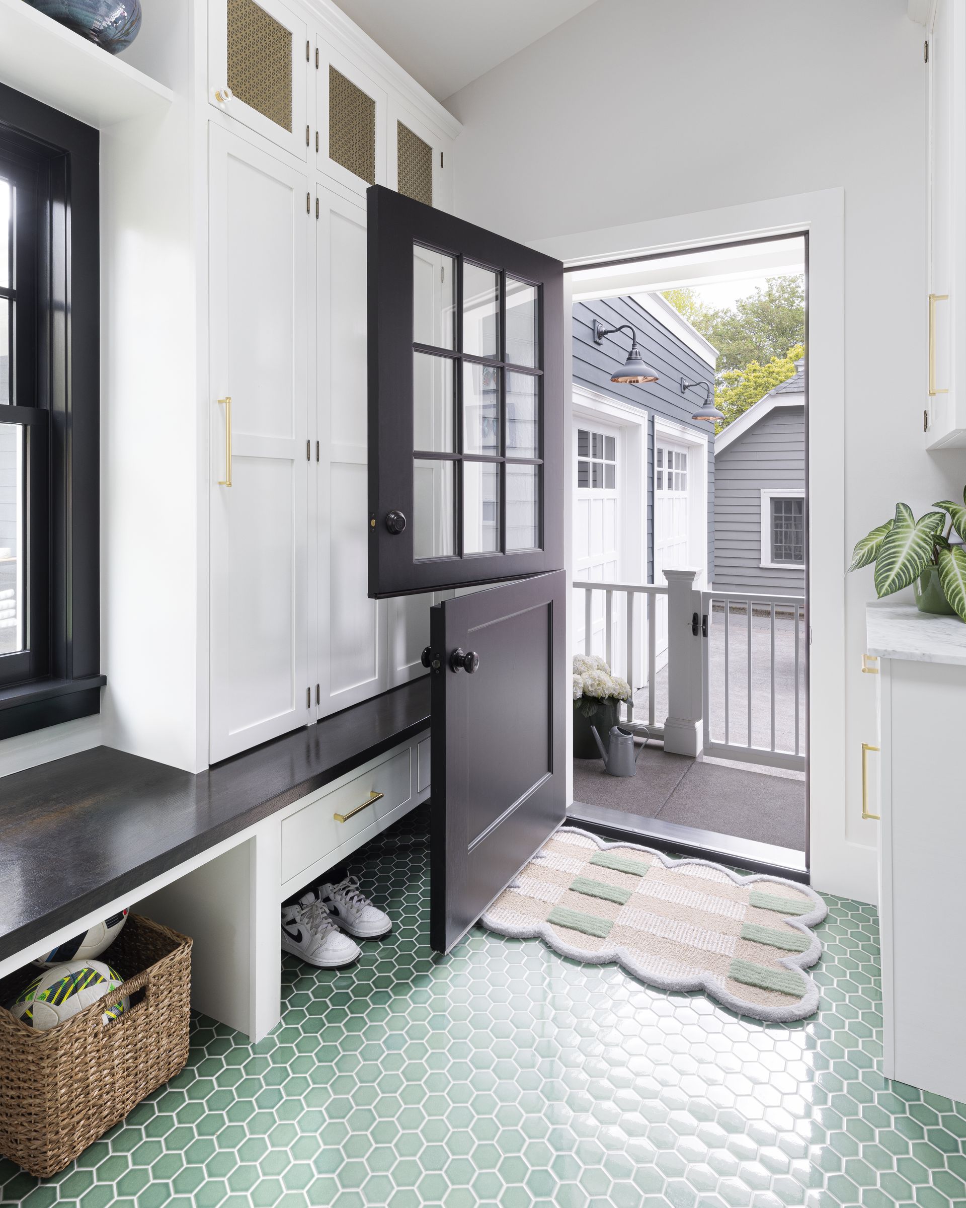 The new bright mudroom with grass green floor tile, ample white built ins and black accents at the windows and dutch door.