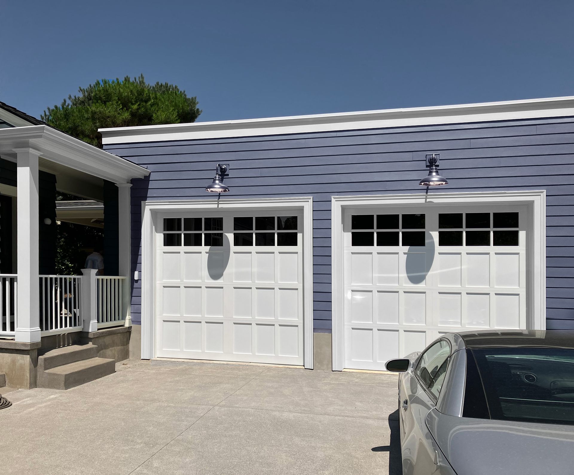 View of the expanded garage from the driveway with the mudroom on the left in blue gray with white doors and trim.