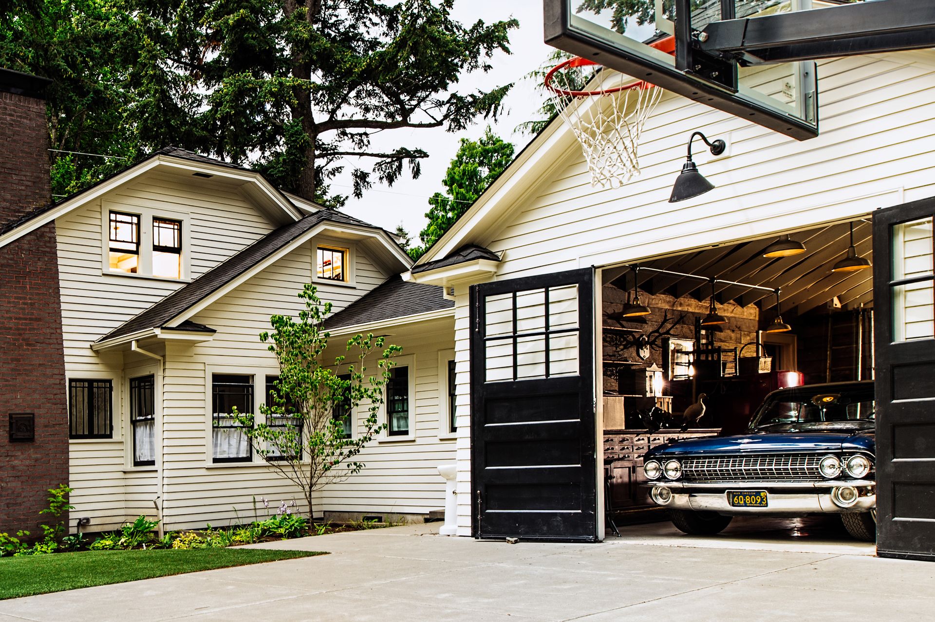 Under towering conifers, the remodeled 1920 bungalow now connects to the garage, with its black carriage doors open.