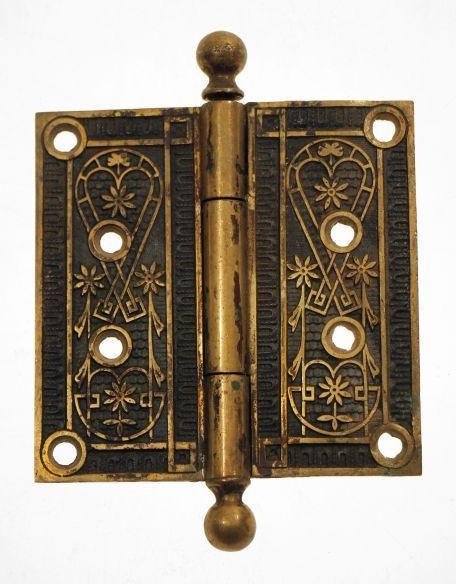 Ornate brass door hinge with floral cutout detailing and round finials
