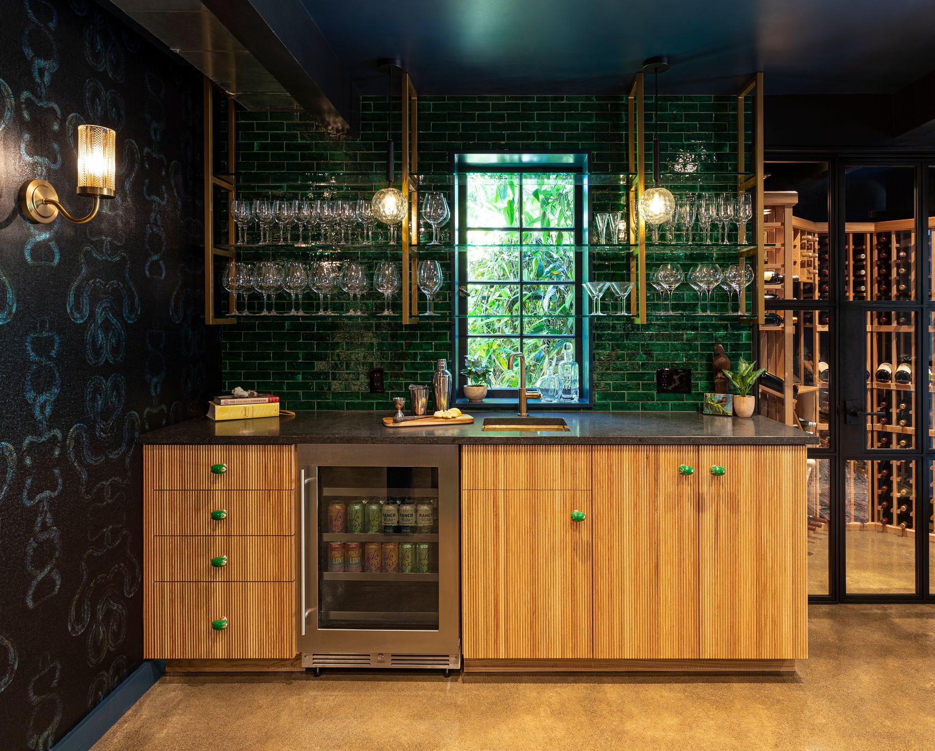 Custom basement bar with tambor front cabinets and brass shelving contrasts with deep-hued wallpaper and tile.