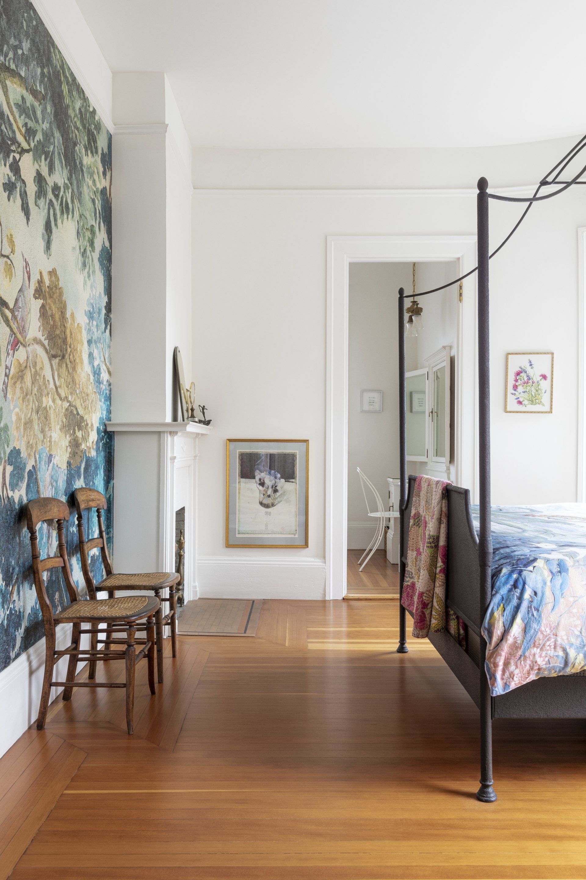 Bedroom with fir floors, a wallpaper mural by Anthropologie, a wrought iron bed and a small fireplace in the corner.