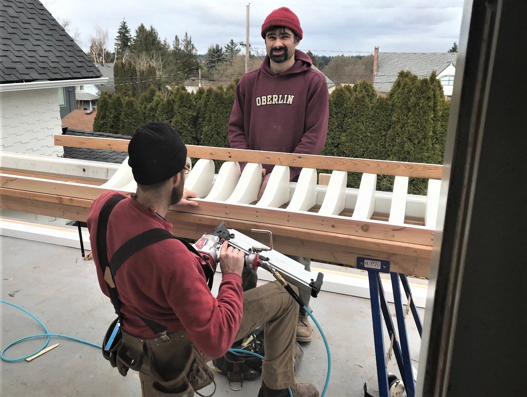 Two men are working on a wooden railing on a roof.