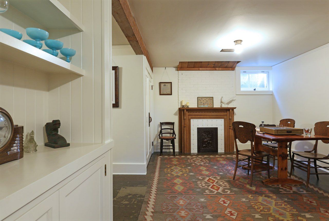 The  remodeled basement family room has a salvaged fireplace surround and screen, a large vintage rug and white walls and ceiling.
